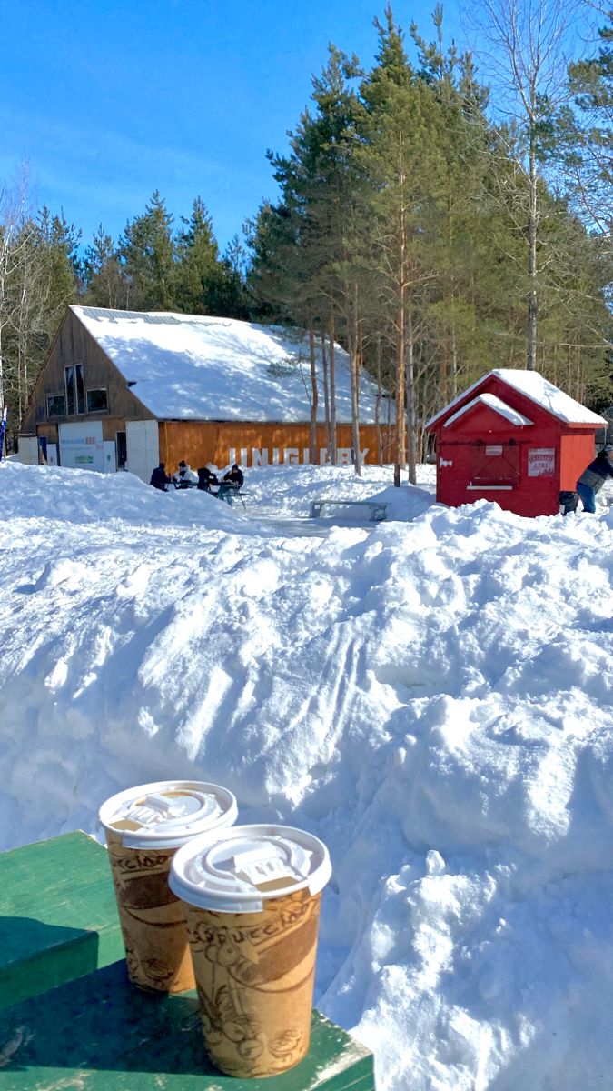 two coffee cups sitting on top of a table covered in snow next to a red barn