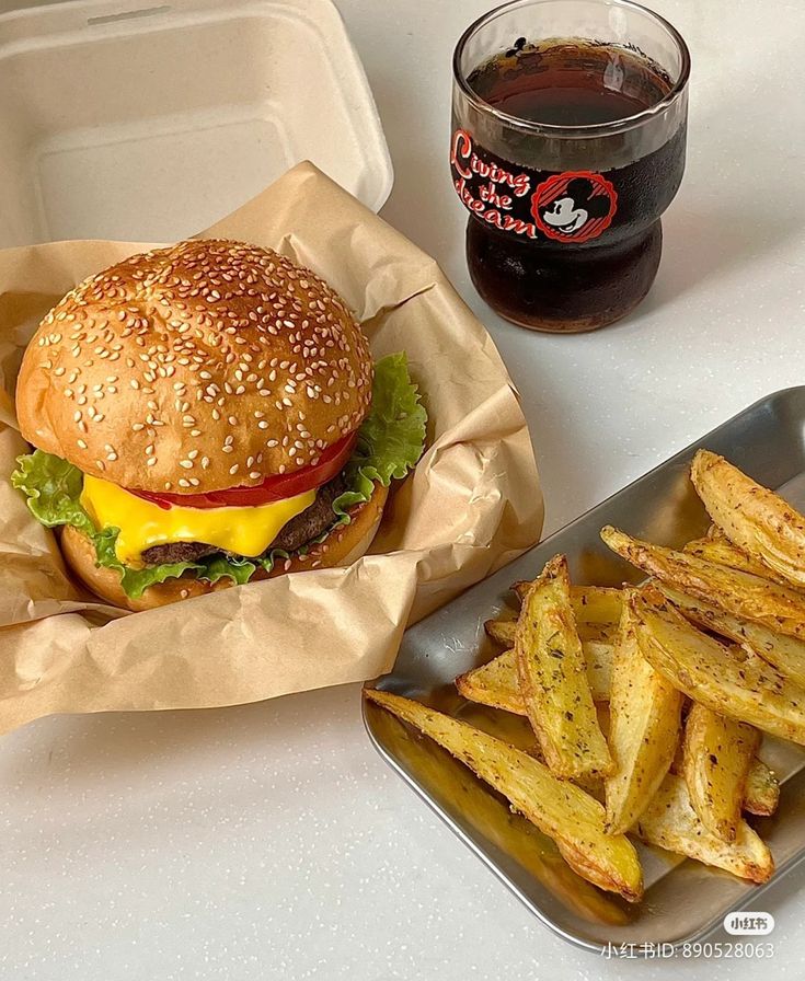 a hamburger and french fries on a tray next to a cup of soda or cola