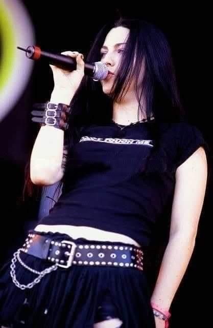 a woman with long black hair is singing into a microphone and holding a chain around her waist