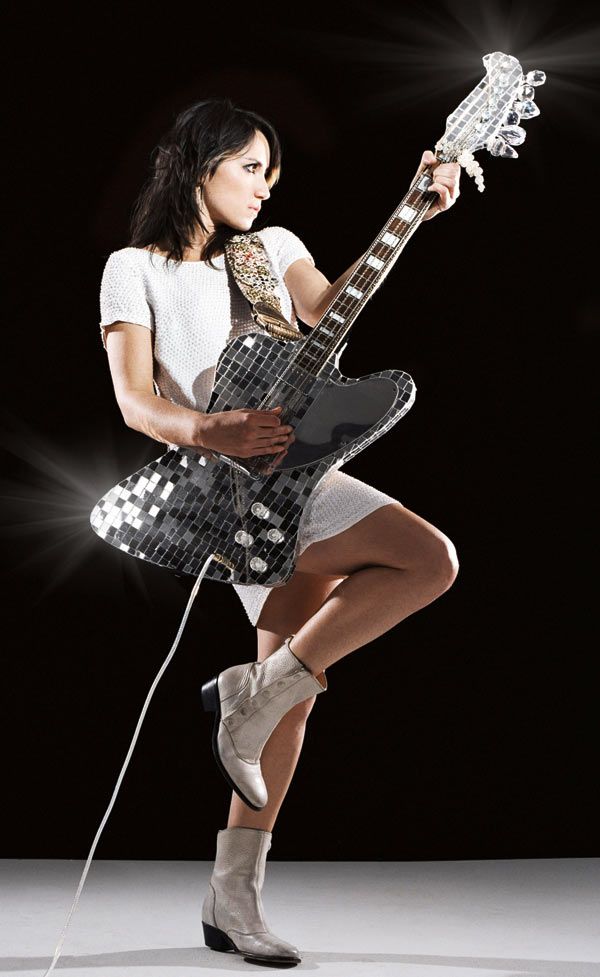 a woman in short shorts and boots holding an electric guitar on a black background with lights