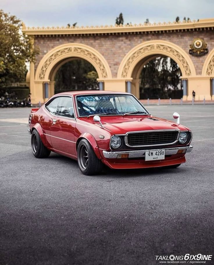 an old red car parked in front of a building