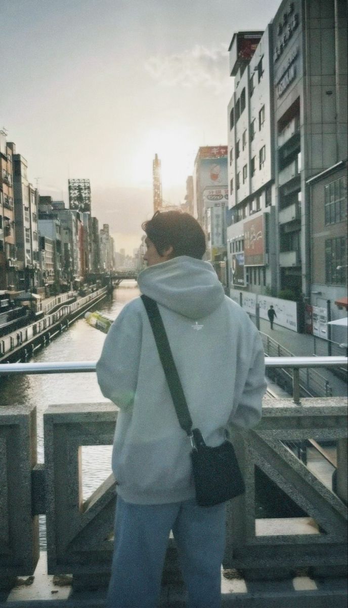 a person is standing on a bridge looking at the water and buildings in the distance