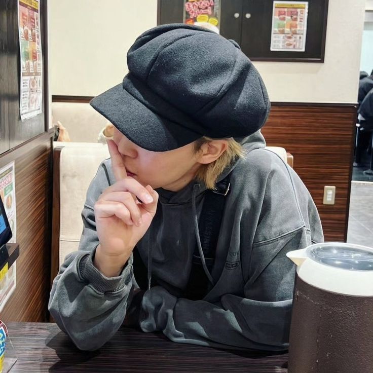 a woman sitting at a table with a cell phone in her hand and wearing a hat