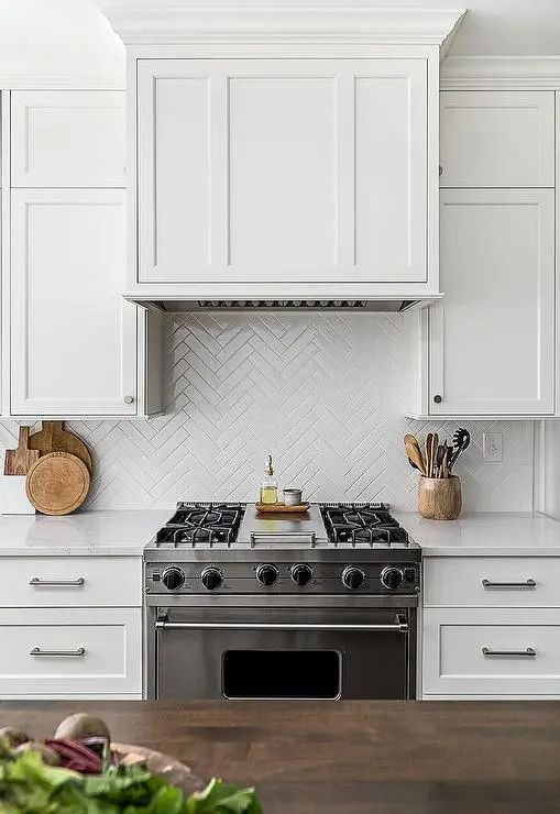 a kitchen with white cabinets, an oven and a cutting board on the counter top