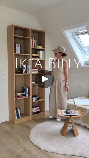 a woman standing in front of a book shelf next to a white couch and chair