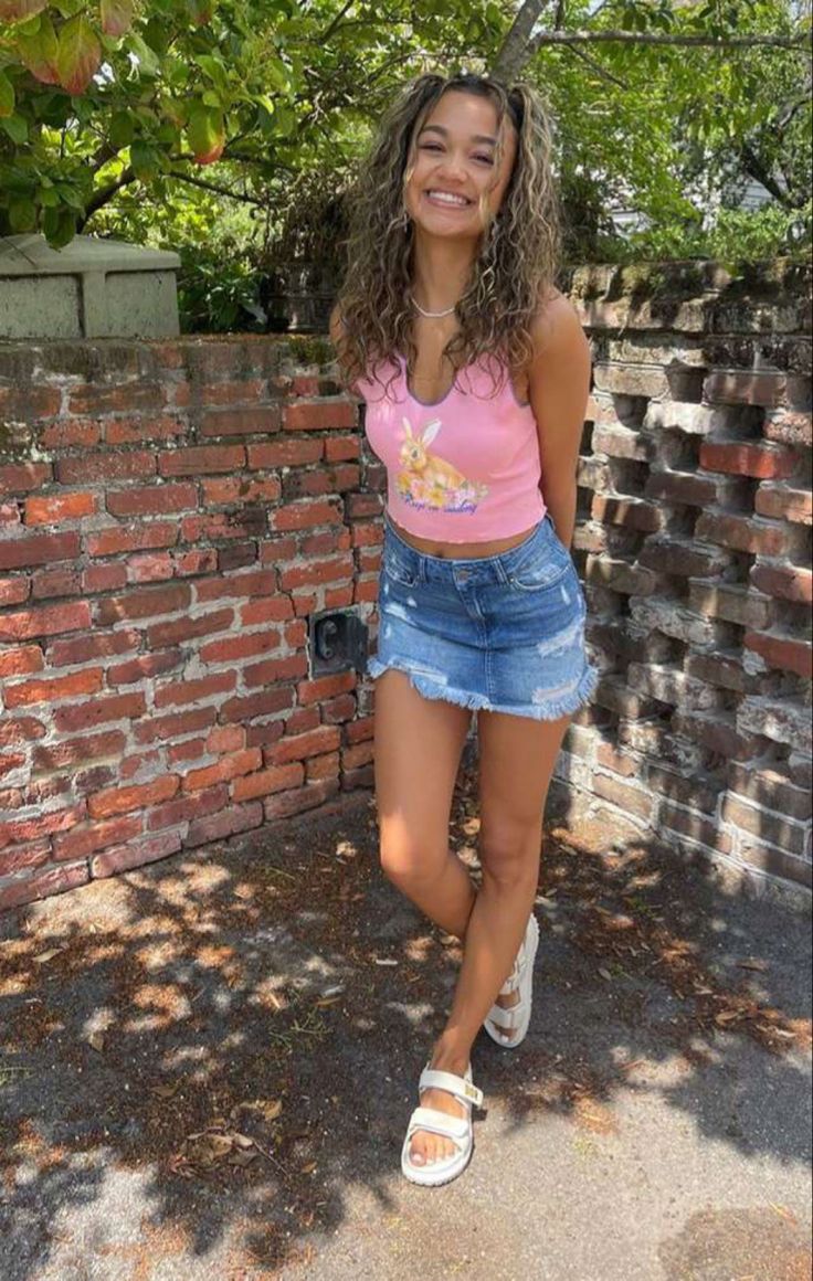 a woman standing next to a brick wall and smiling at the camera with her hands in her pockets