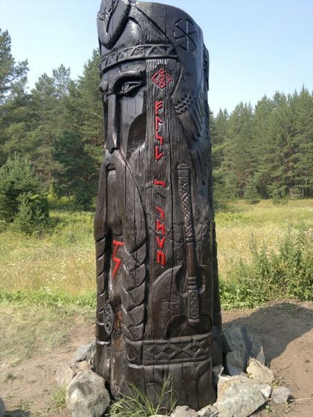 a large wooden statue sitting on top of a lush green field next to a forest