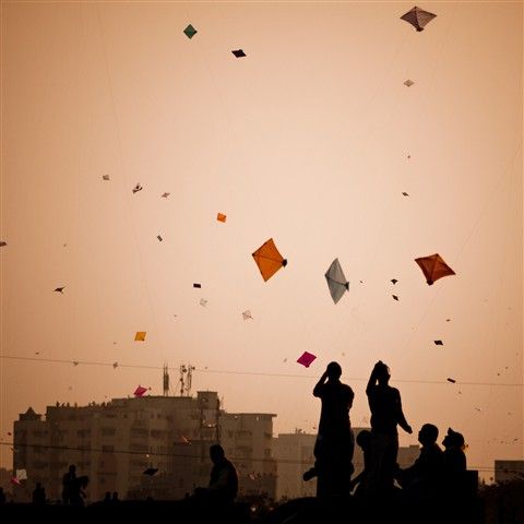 silhouettes of people flying kites in the sky at sunset or dawn with buildings in the background