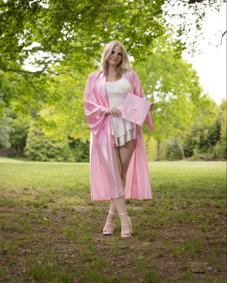 a woman in a pink robe and heels is walking through the grass with trees behind her