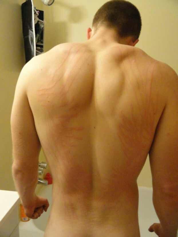 a man with no shirt standing in front of a bathroom mirror looking at his back