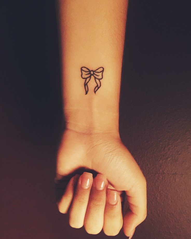 a woman's wrist with a small bow tattoo on the left side of her arm