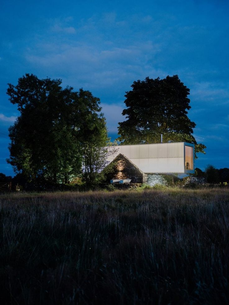 a house in the middle of a field with trees and grass around it at night