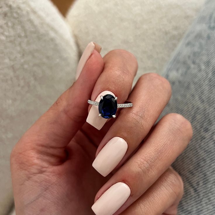 a woman's hand holding a ring with an oval blue stone on it