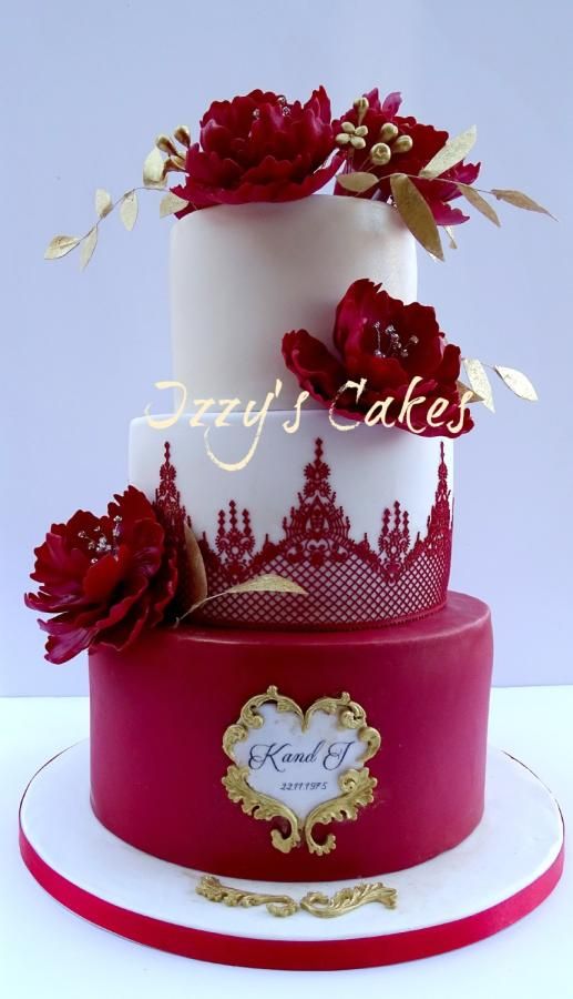 a three tiered cake with red flowers on the top and gold trimmings