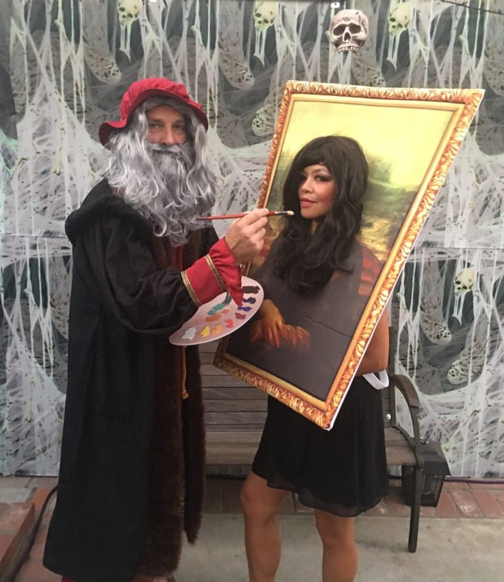 a man dressed as santa claus holding up a painting with a woman in the background