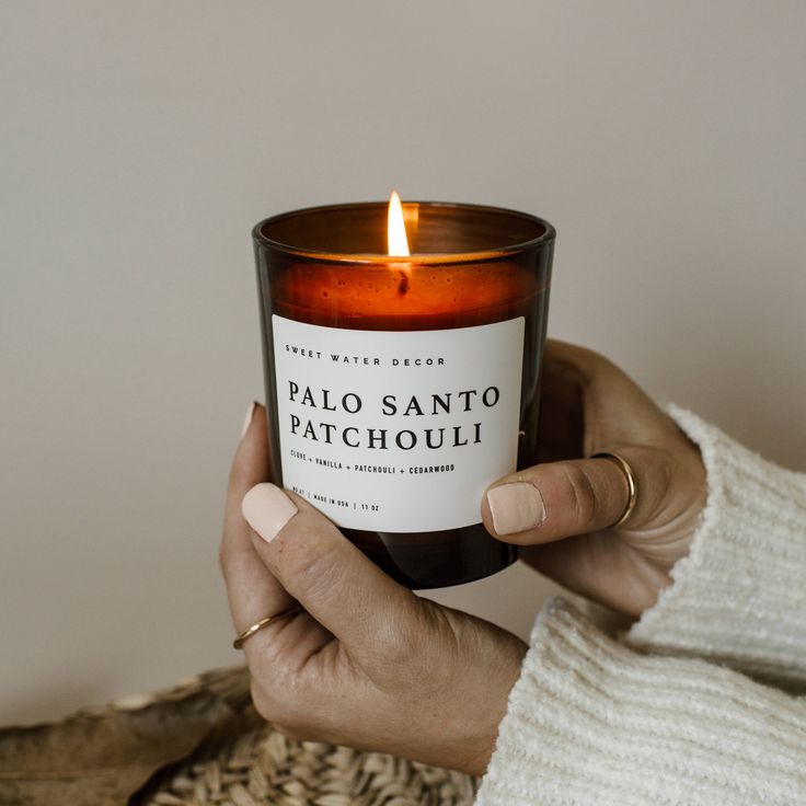 a woman holding a candle in her hand with the words palo - santo patchoui on it