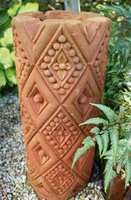 a planter sitting on top of a gravel ground next to a green fern tree