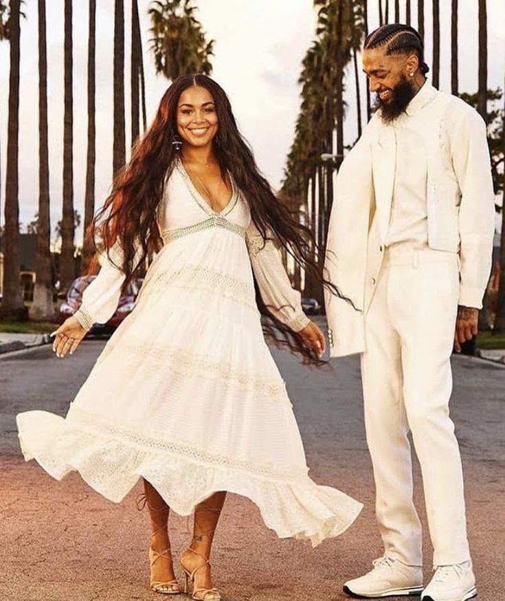 a man and woman standing in the middle of a street with palm trees behind them