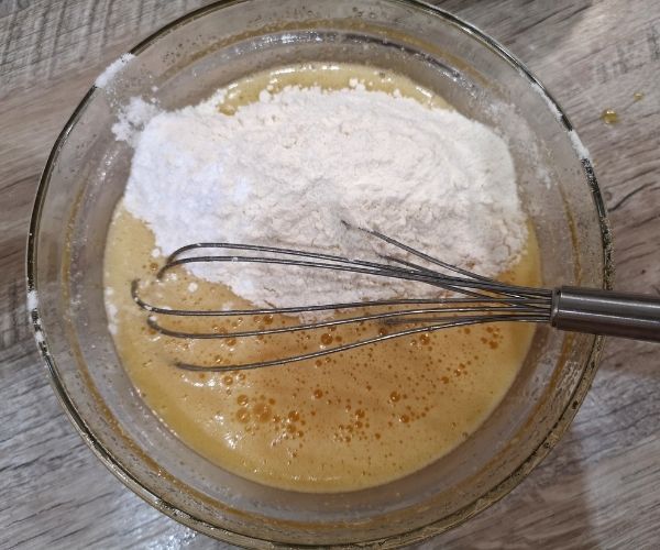 a glass bowl filled with flour and whisk on top of a wooden table