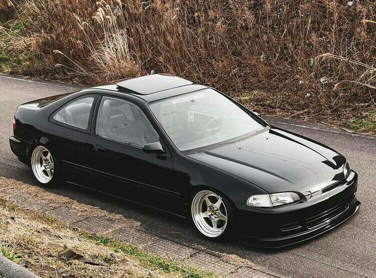 a black car is parked on the side of the road next to some grass and bushes