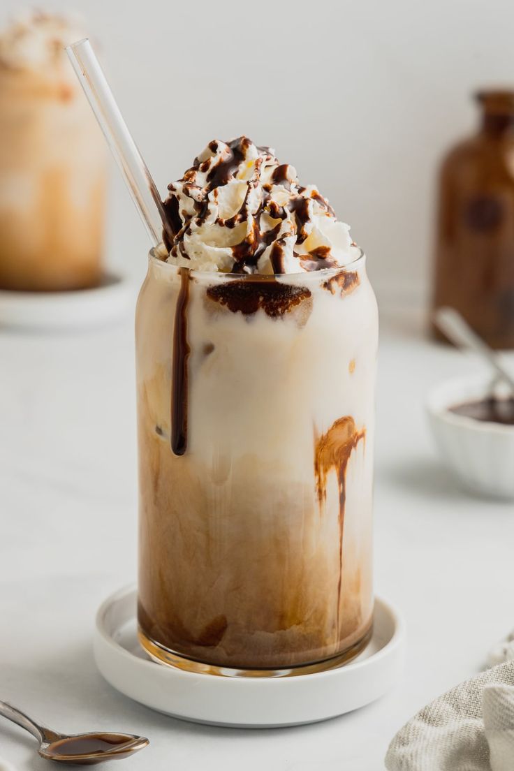 an iced drink with whipped cream and chocolate drizzled on top, sitting on a white plate