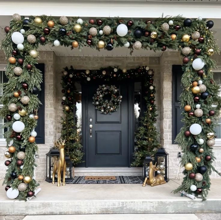 a front porch decorated for christmas with ornaments and greenery on the door, along with two gold deer statues