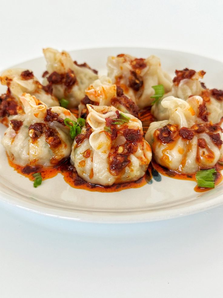 some dumplings are sitting on a white plate with sauce and green garnish