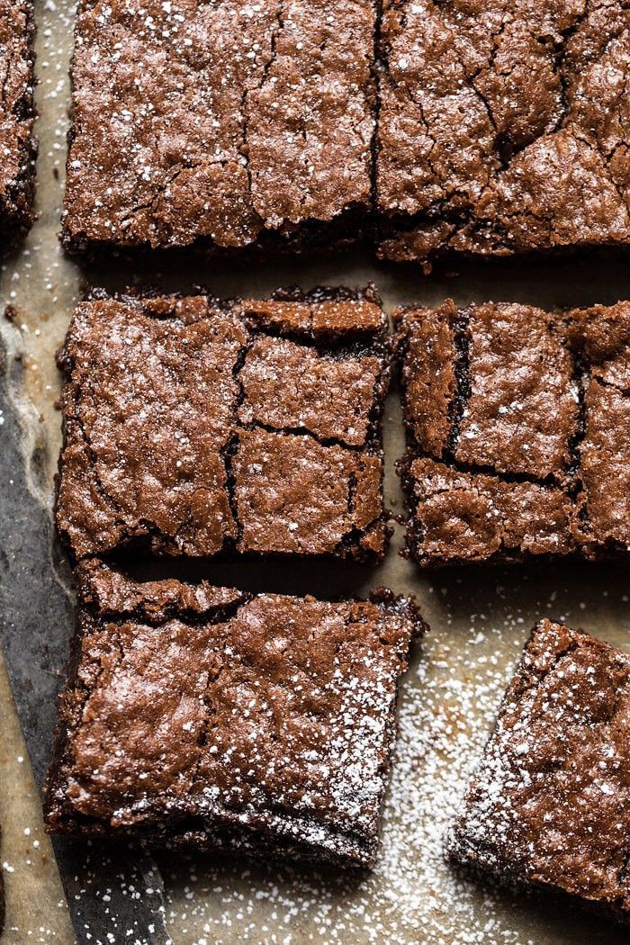 chocolate brownies with powdered sugar arranged on a baking sheet next to a spatula