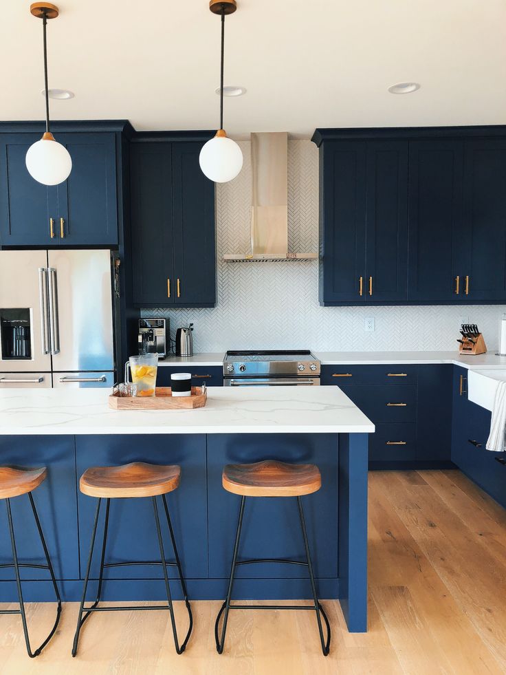 a kitchen with blue cabinets and stools next to an island in the middle of the room