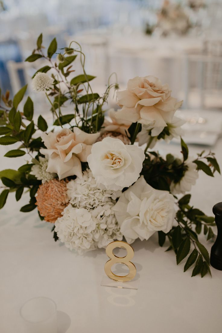 a bouquet of flowers and two wedding rings on a table with white chairs in the background