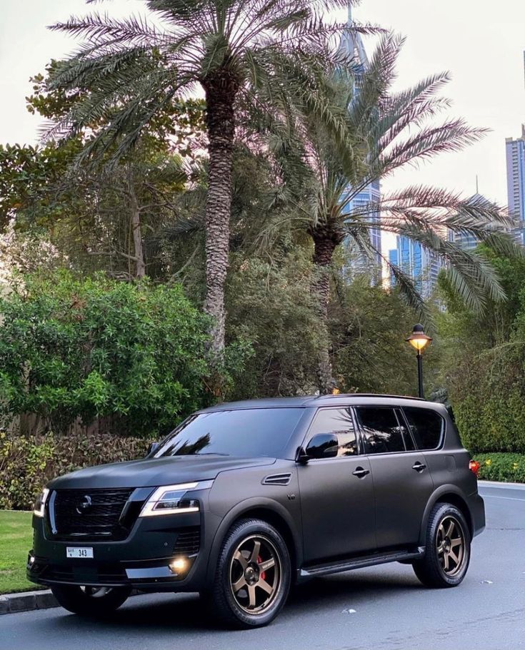 a black suv is parked on the street in front of some palm trees