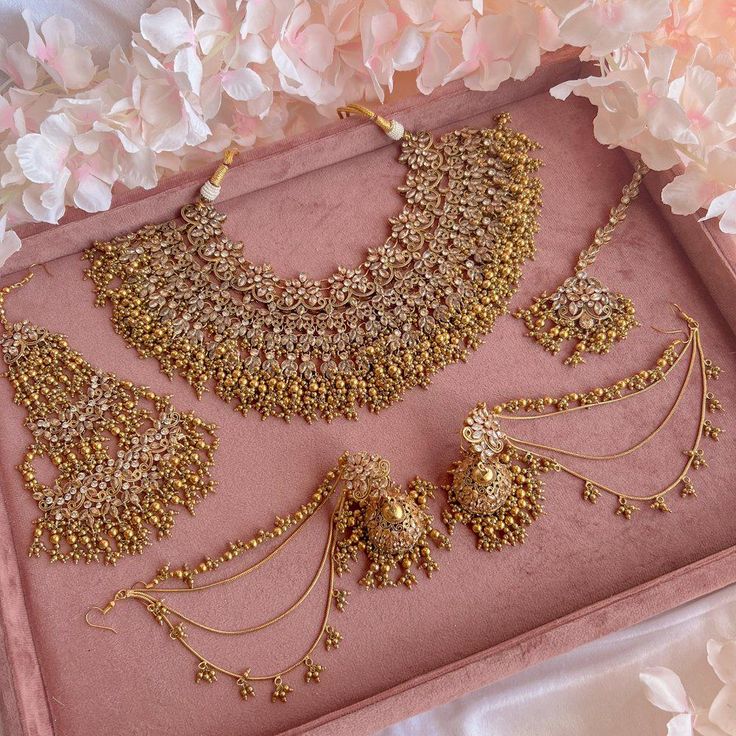 a pink tray with some gold jewelry on it and flowers in the backgroud