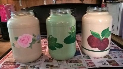 three glass jars sitting on top of a newspaper with flowers painted on the lids and sides