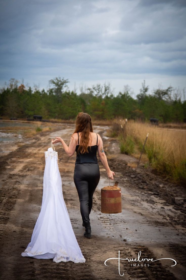 a woman walking down a dirt road holding a wedding dress