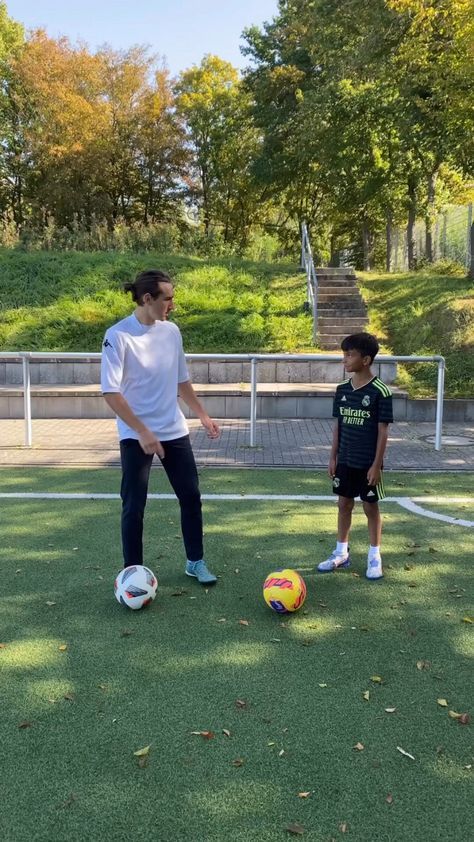 a man standing next to a little boy on top of a soccer field with a ball