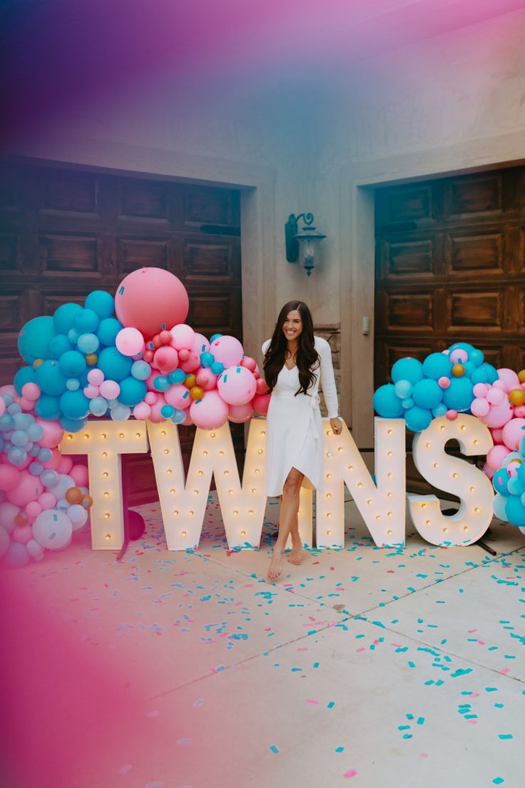 a woman standing in front of a sign that says twins with balloons and confetti