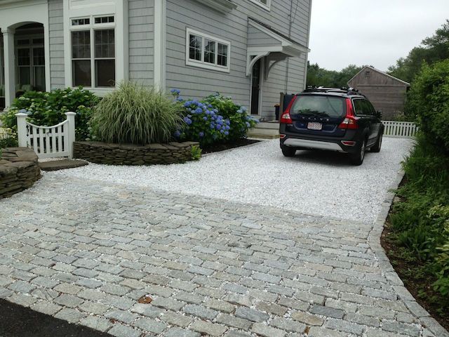 a car is parked in front of a house with gravel driveway and landscaping around it