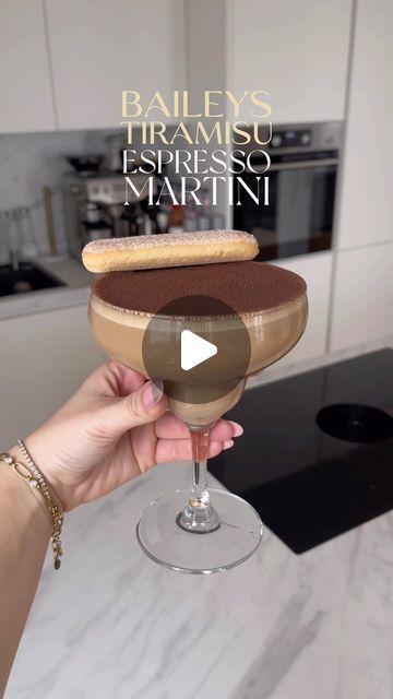 a person holding a wine glass with a cookie in it and the words bailey's tramsu espresso martini