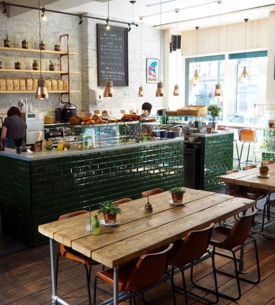 the inside of a restaurant with wooden tables and chairs, green brick walls, and lots of potted plants