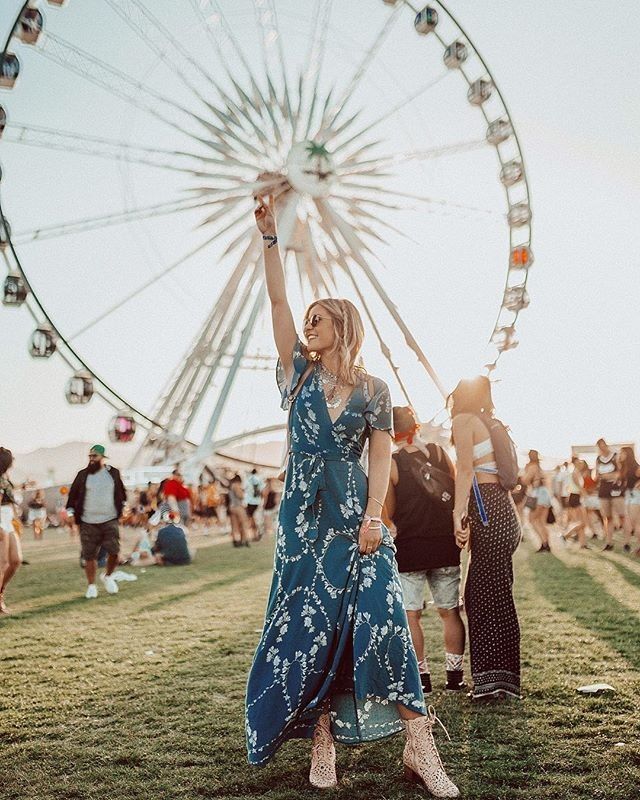 a woman standing in front of a ferris wheel at a music festival with her hand up