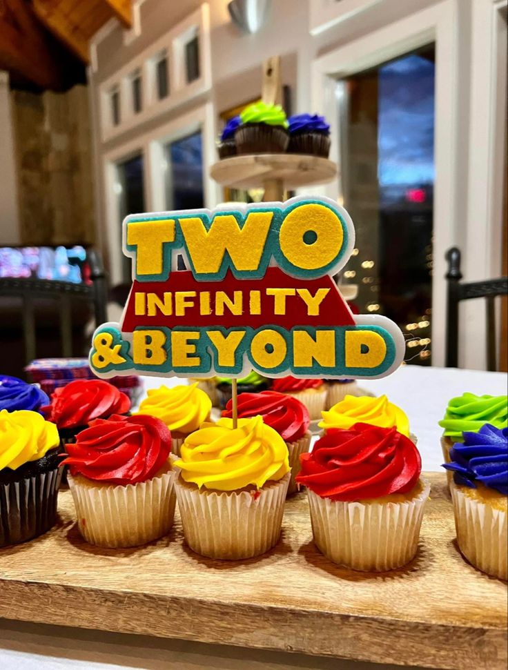 cupcakes with colorful frosting are on a wooden tray in front of a sign that says two infinitely and beyond