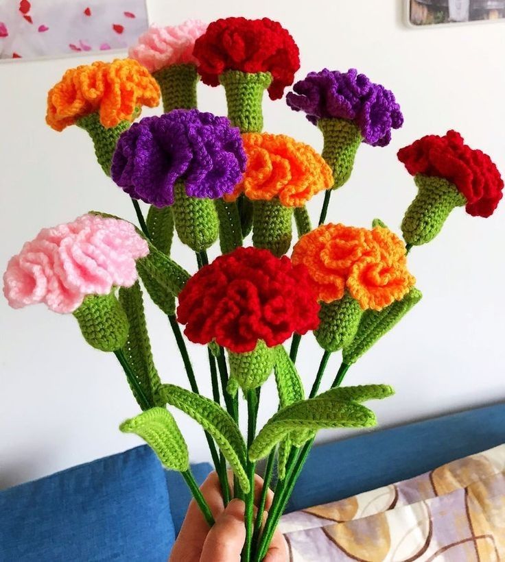 a hand holding a bunch of crocheted flowers in front of a wall with pictures on it