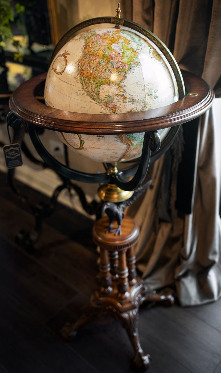 an old world globe is sitting on top of a stand in front of a window