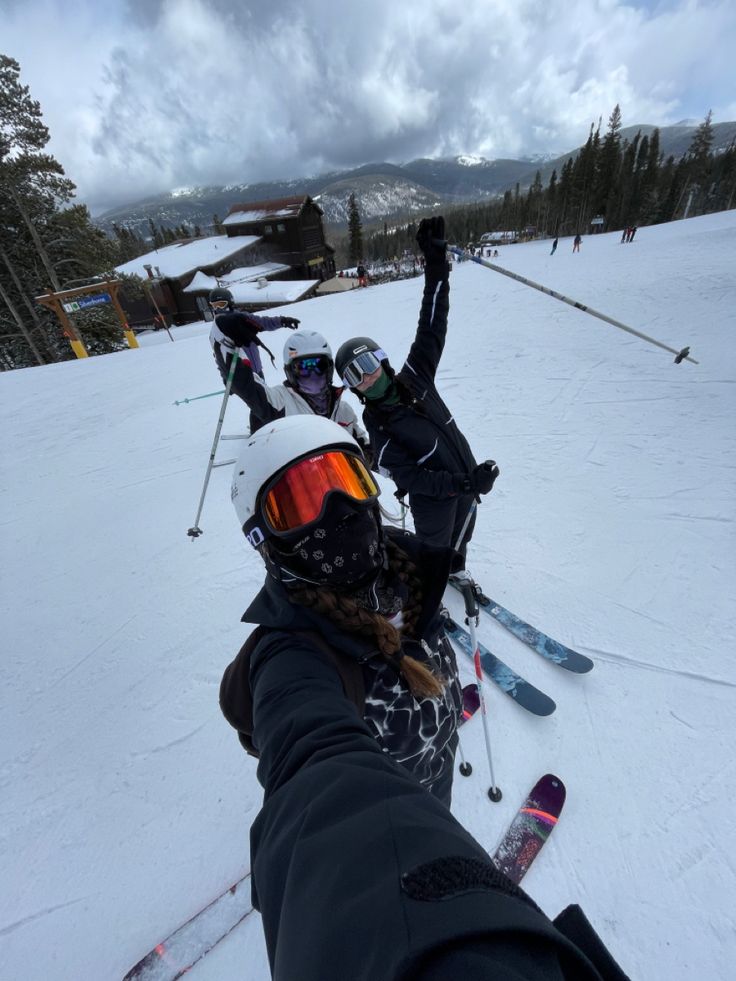 two skiers pose for the camera on a snowy mountain slope with their arms in the air