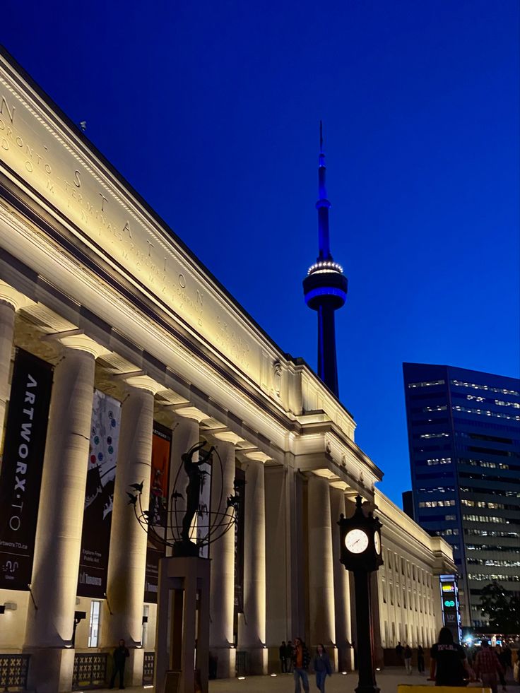 the building is lit up at night with people walking around