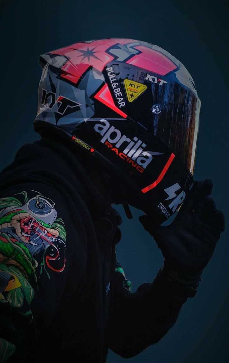 a person wearing a helmet and holding his hand up to their face while standing in front of a dark background