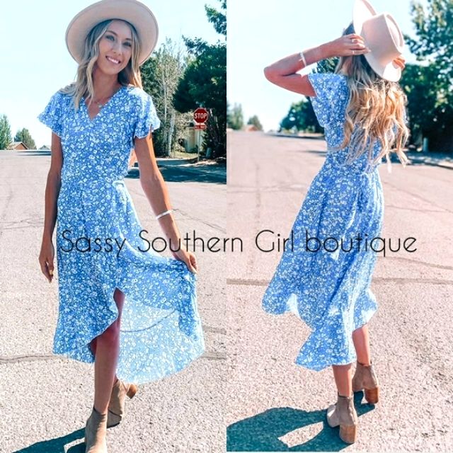 a woman in a blue dress and hat is standing on the street with her hands behind her head