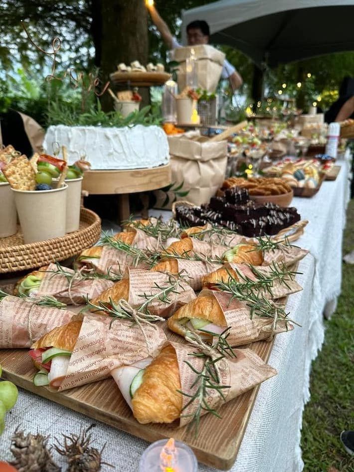 an assortment of food is laid out on a long table with white clothed cloths