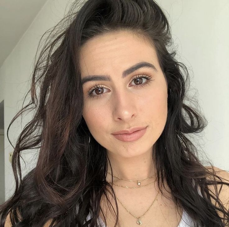 a close up of a person with long hair wearing a white shirt and gold necklace