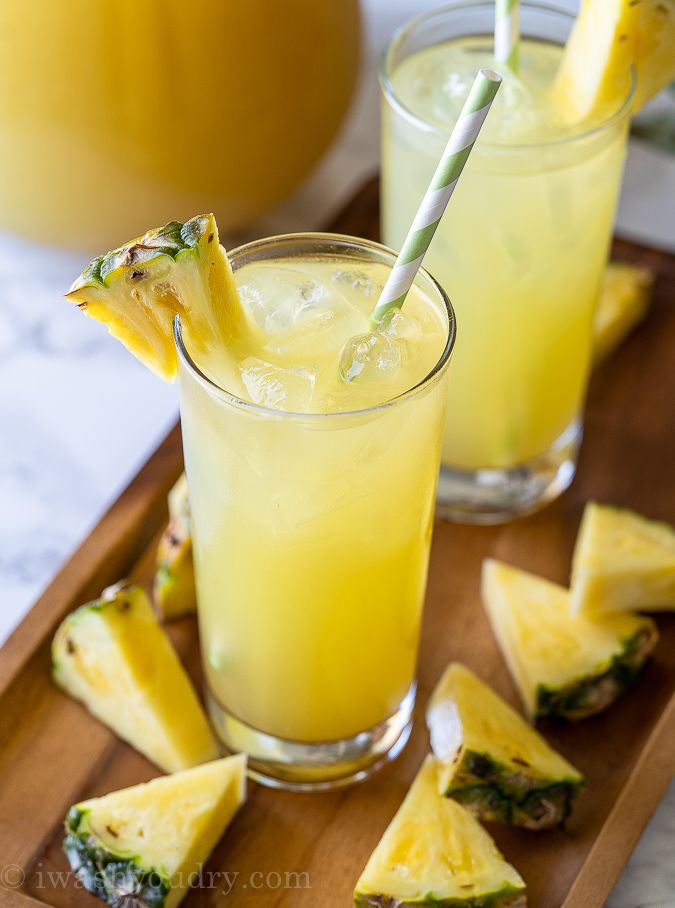 two glasses filled with pineapple juice on a wooden tray